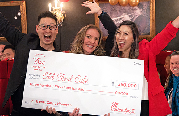 A woman from the S. Truett Cathy Honoree, Old Skool Café, holding a large check and standing next to two other people