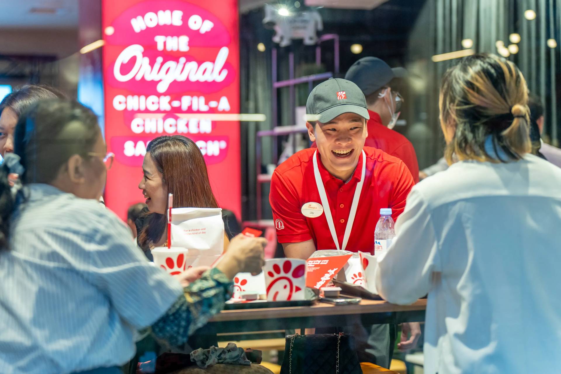 Team member wearing red and smiling while serving guests in a restaurant