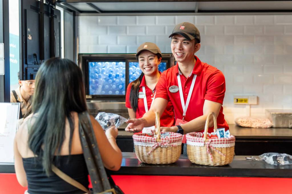 Chick-fil-A team members in red uniforms smile and assist a customer at a counter with wicker baskets.