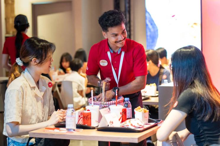 Chick-fil-A employee smiling and interacting with two guests seated at a table.