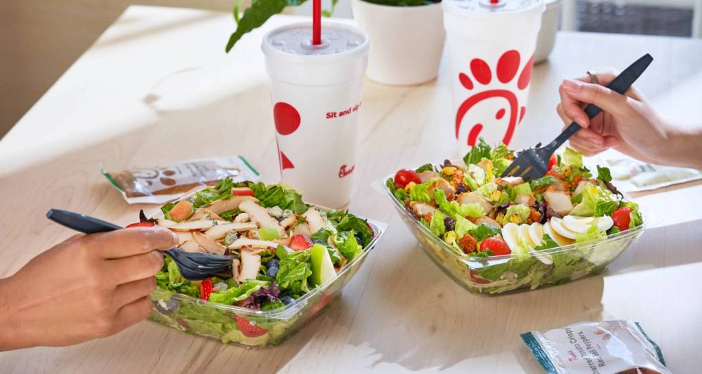 Two salads with chicken and two large cups with the Chick-fil-A logo on a table.